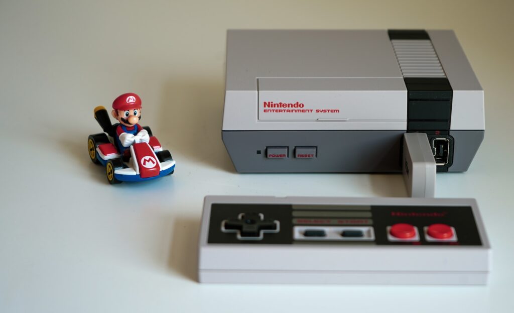 Photograph of an old video game console, its controller, and a Mario Kart action figure.