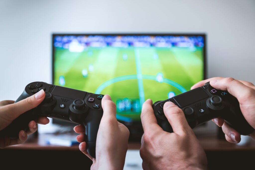 Photograph of two people holding a PlayStation controller while playing a soccer game.

What is crossplay?